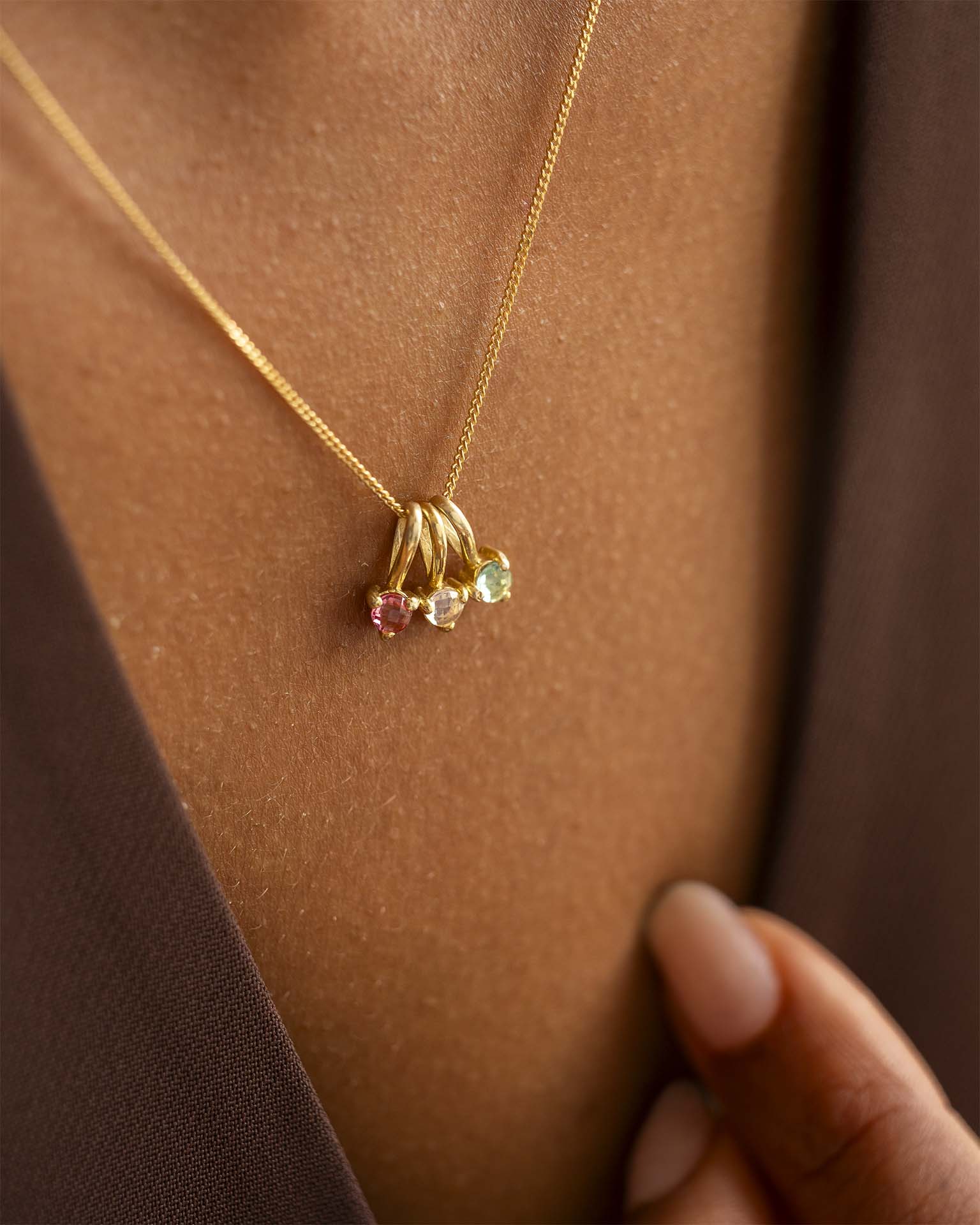 Gold necklace with three colourful gemstones worn on a person's neck.