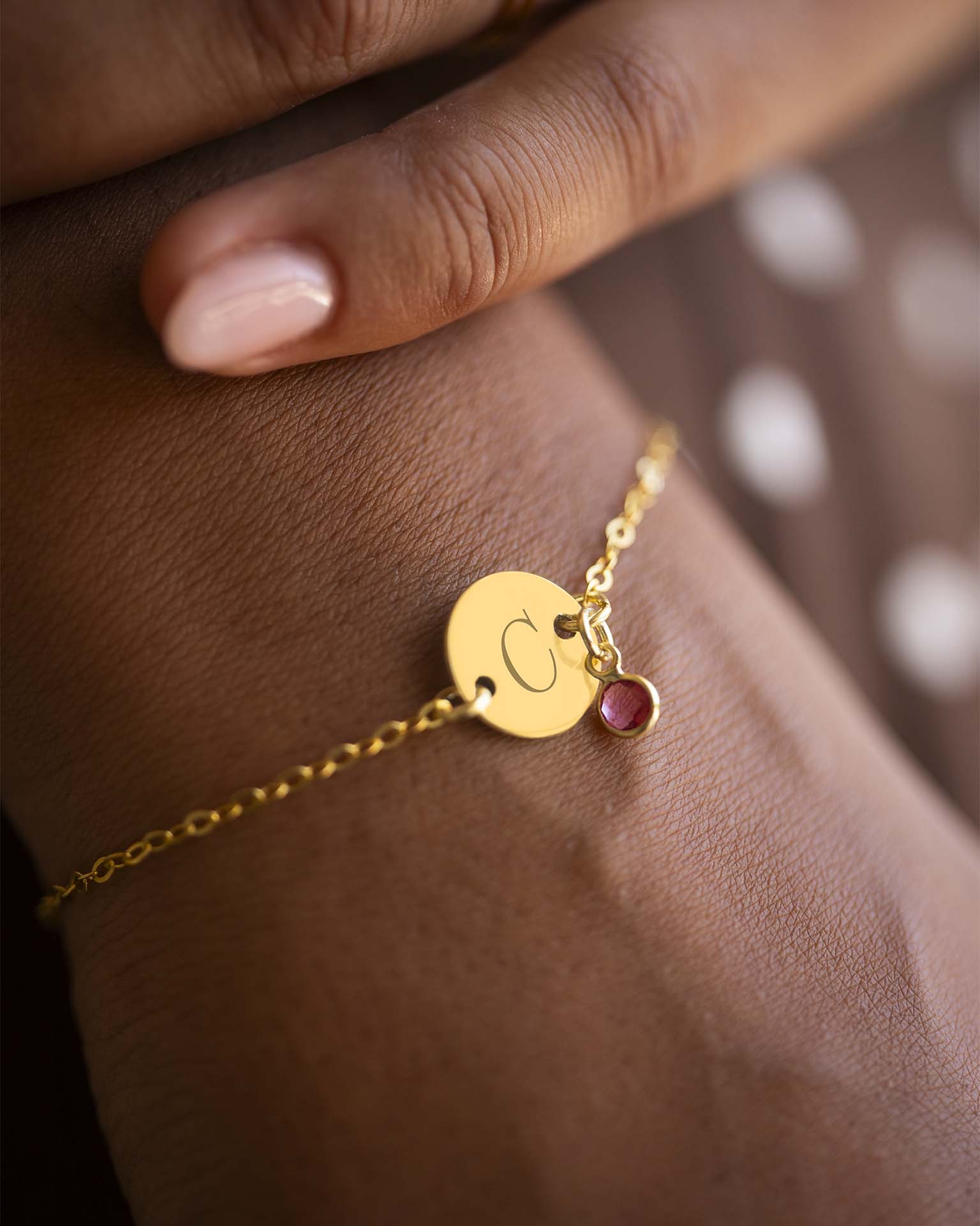 Gold bracelet with a round charm and red gemstone on a wrist. | Christmas