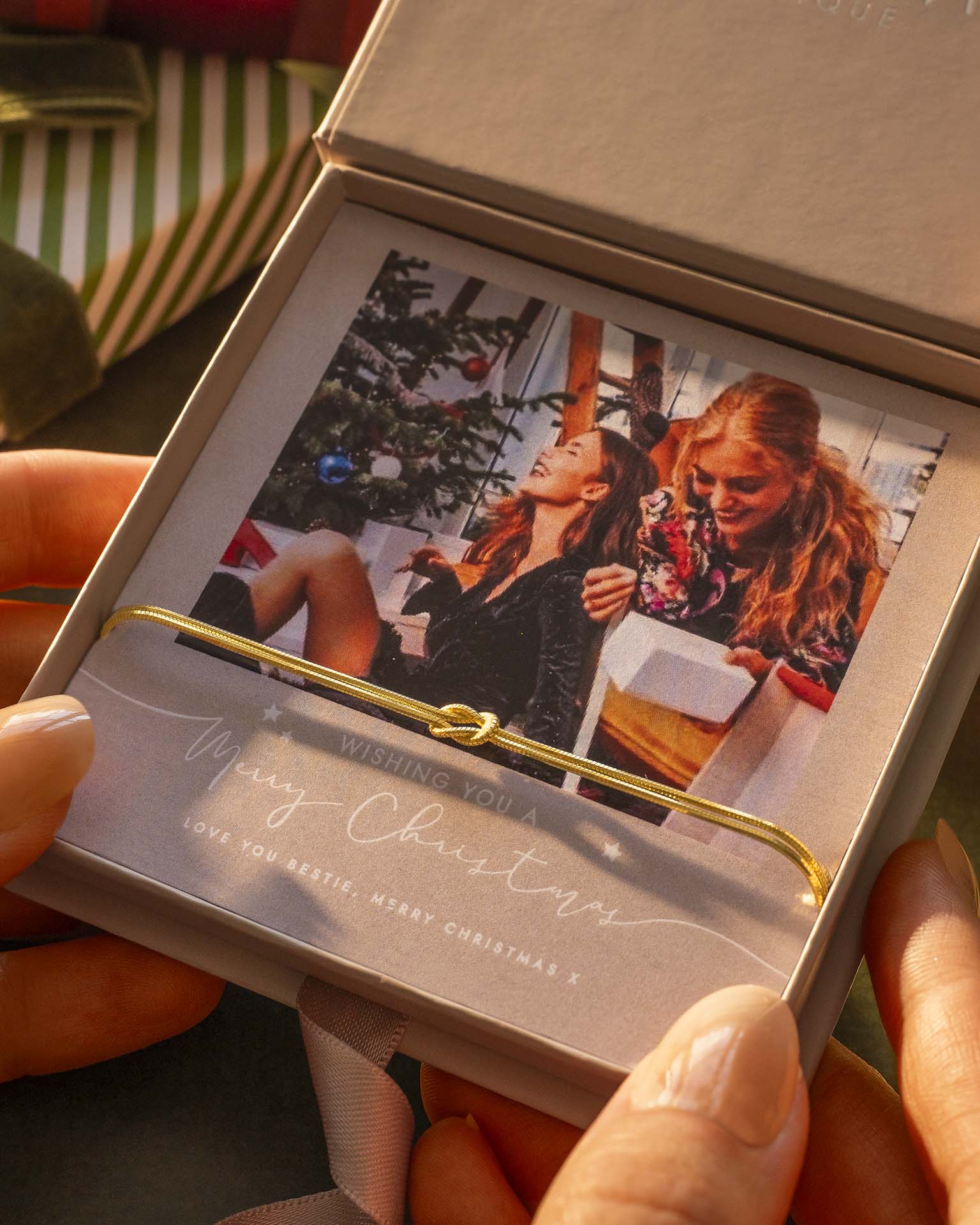Person holding a Christmas card with two people and a tree, inside an open box. | Christmas