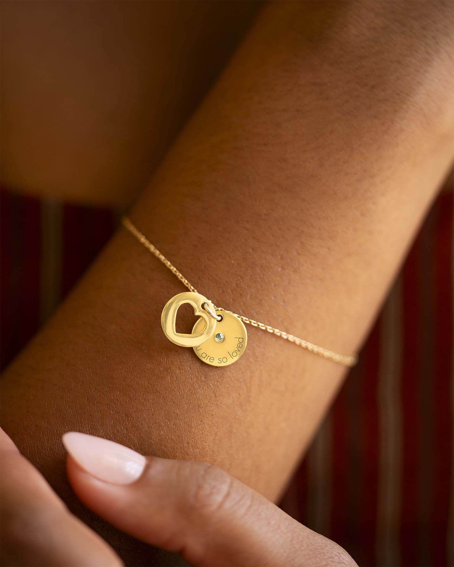 Gold bracelet with heart and round charm on a wrist against a blurred background | Christmas