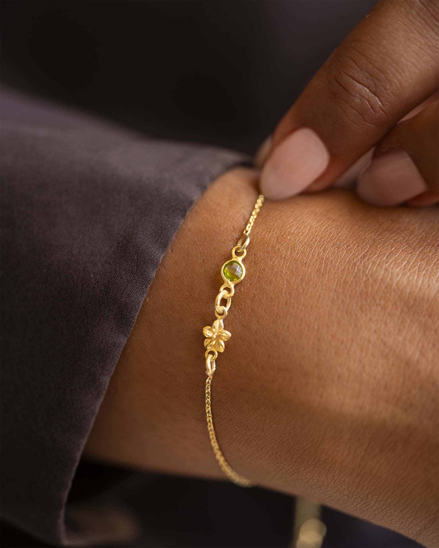Gold bracelet with a green gemstone on a wrist against a dark background | Christmas