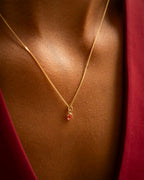 Gold necklace with a red pendant on a person wearing a red garment. | Christmas