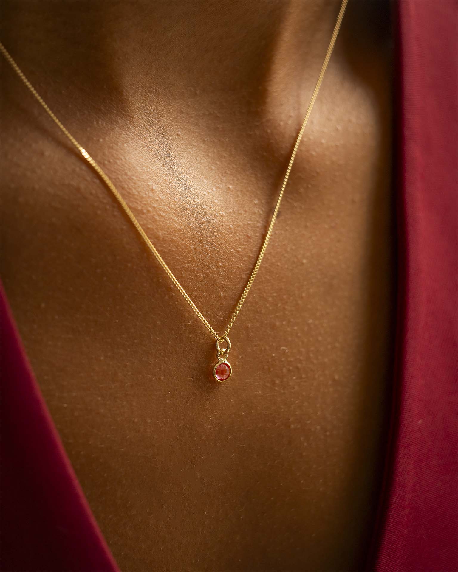 Gold necklace with a red pendant on a person wearing a red garment. | Christmas