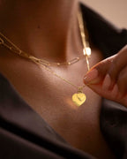 Gold necklace with heart-shaped pendant being adjusted on a person's neck.
