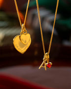 Two gold necklaces with heart-shaped and letter 'A' pendants on a blurred background.