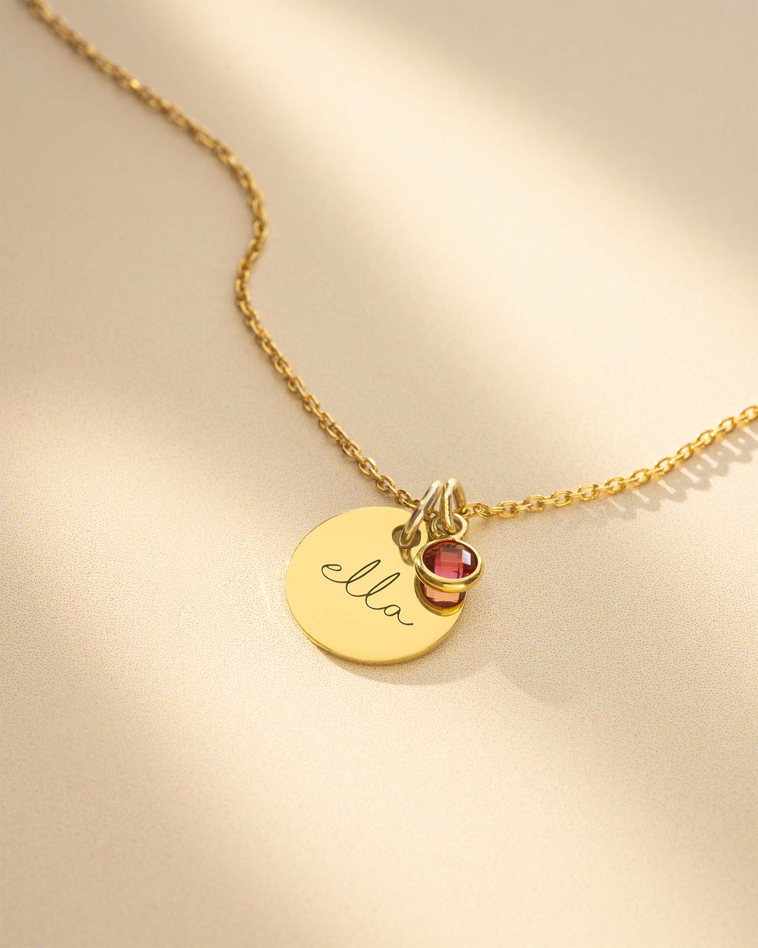 Gold necklace with a round pendant and heart-shaped charm on a beige background