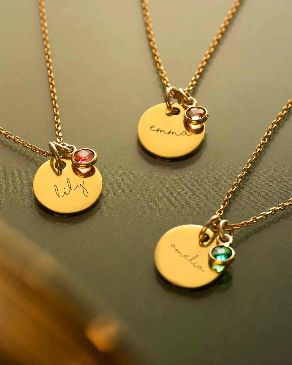 Three gold necklaces with engraved names on round pendants against a green background | Christmas
