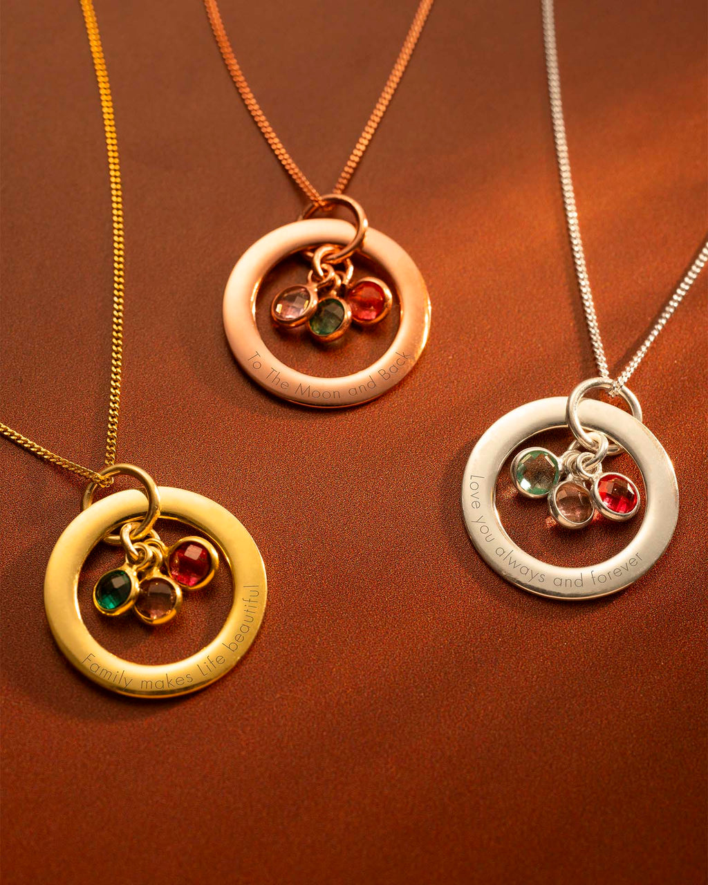 Three circular gold, rose gold, and silver necklaces with embedded gemstones on a brown background.