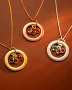 Three circular gold, rose gold, and silver necklaces with embedded gemstones on a brown background.