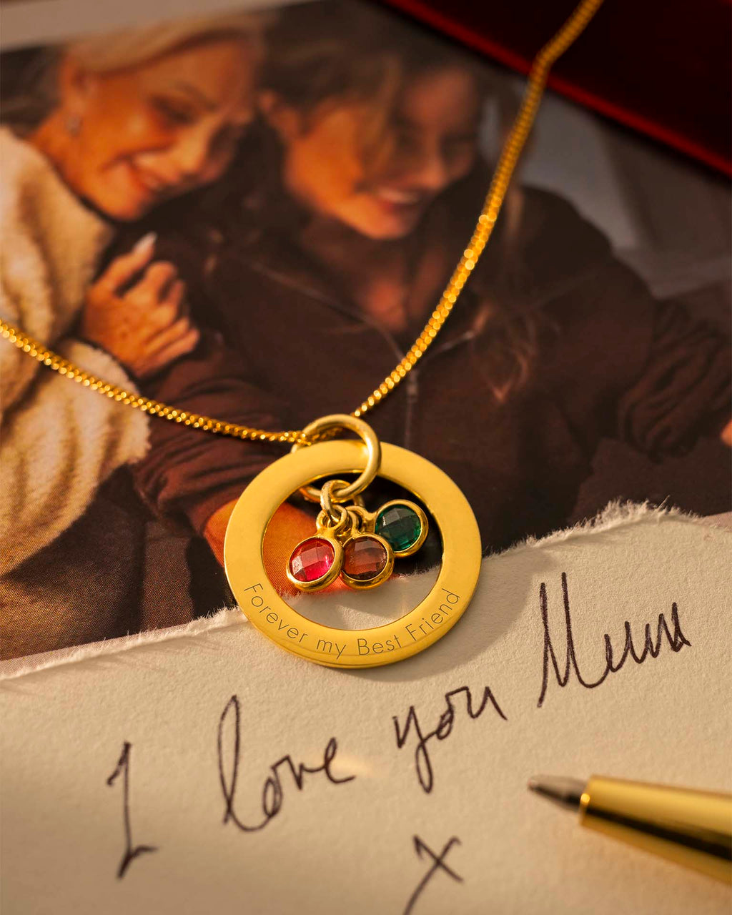 Gold necklace with a pendant on a surface with a handwritten note and photo in the background. |  Christmas