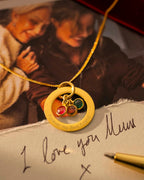 Gold necklace with a pendant on a surface with a handwritten note and photo in the background. |  Christmas