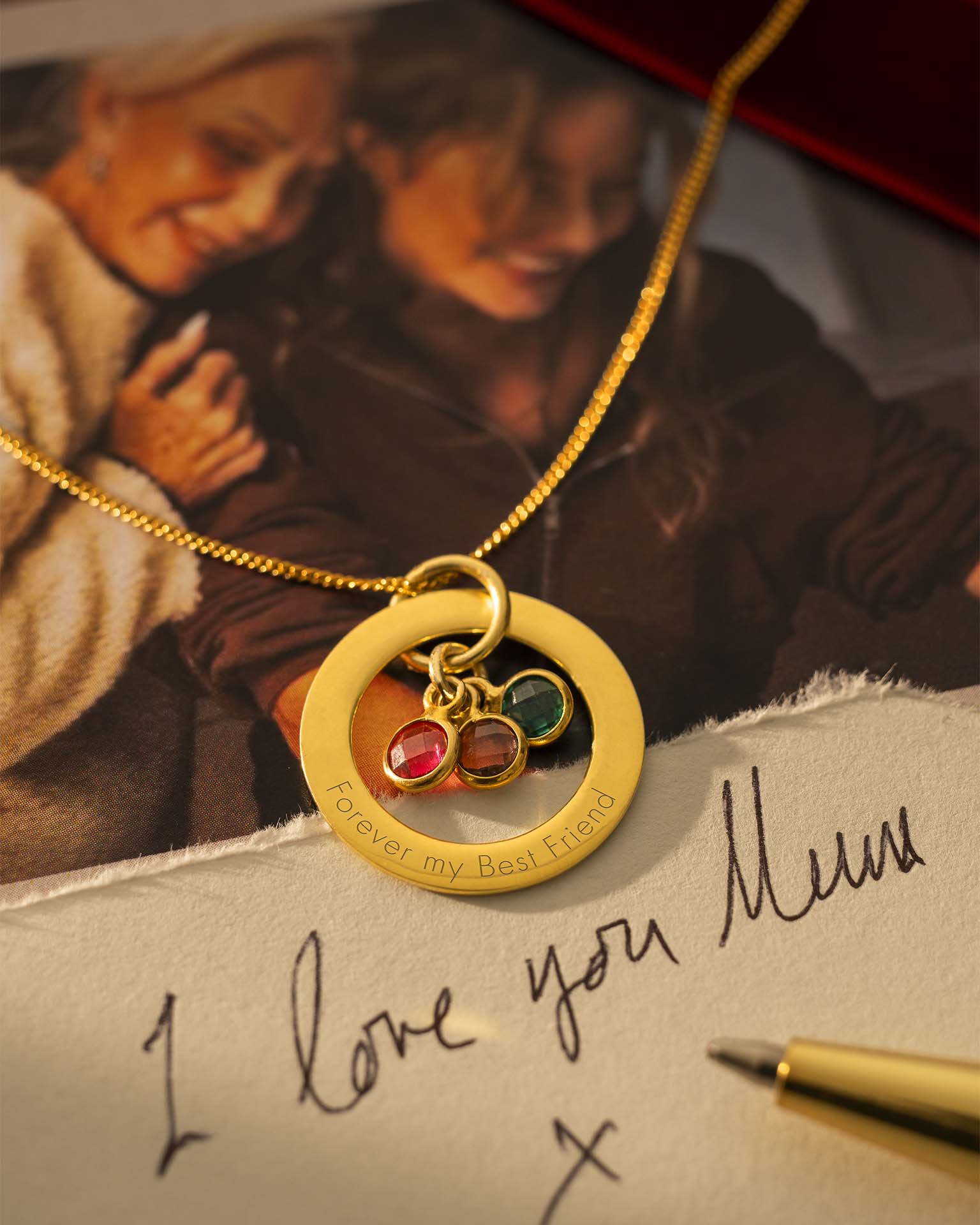 Gold necklace with a pendant on a surface with a handwritten note and photo in the background. |  Christmas
