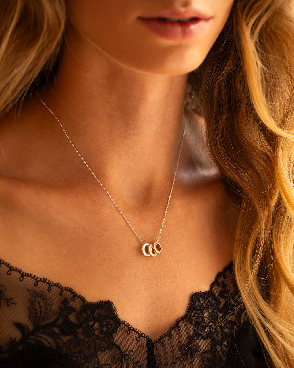 Close-up of a woman wearing a delicate necklace with three interlocking rings, set against a blurred background.