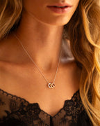 Close-up of a woman wearing a delicate necklace with three interlocking rings, set against a blurred background.
