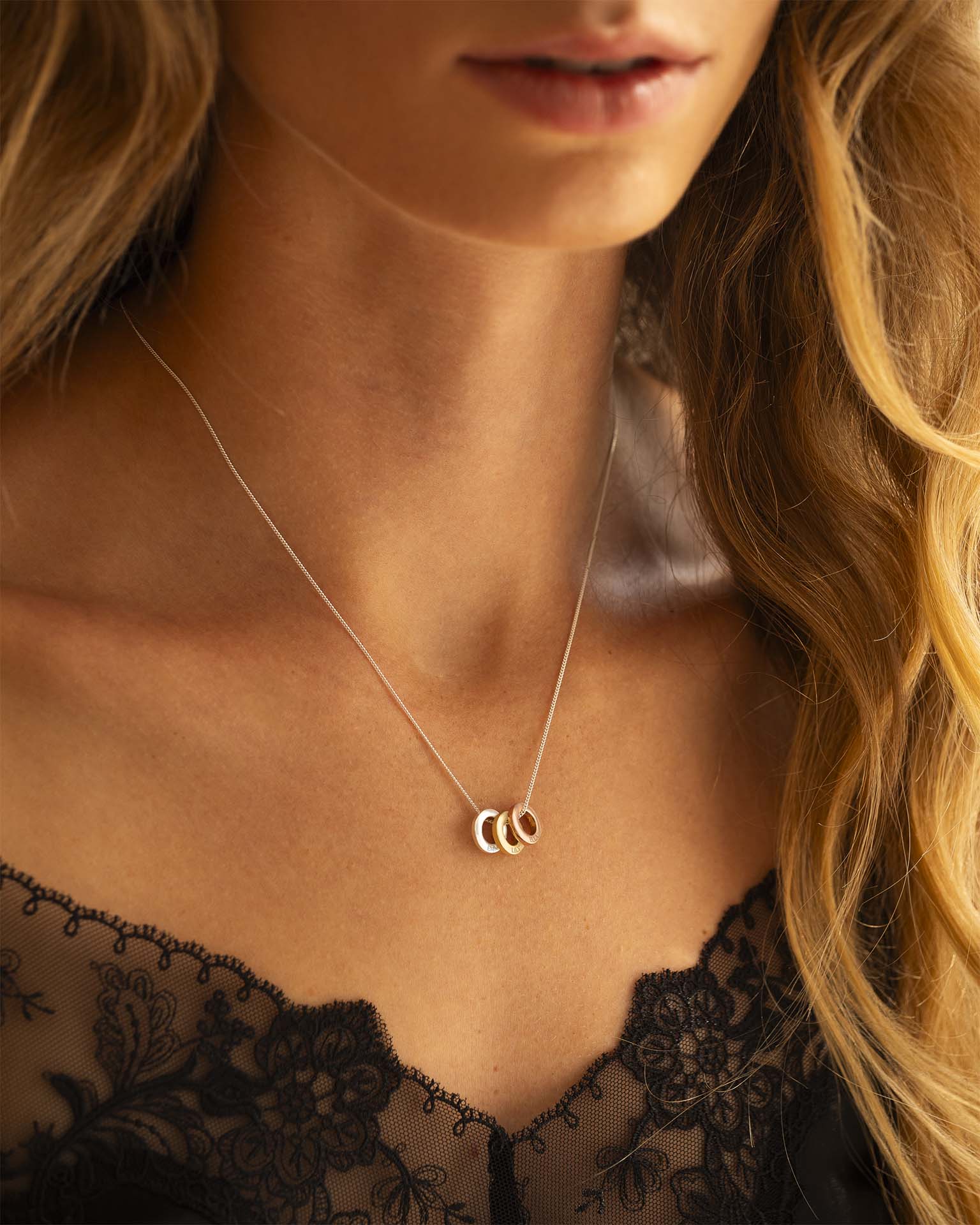 Close-up of a woman wearing a delicate necklace with three interlocking rings, set against a blurred background.