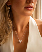 Close-up of a woman wearing a silver necklace with interlocking rings, with a neutral background.