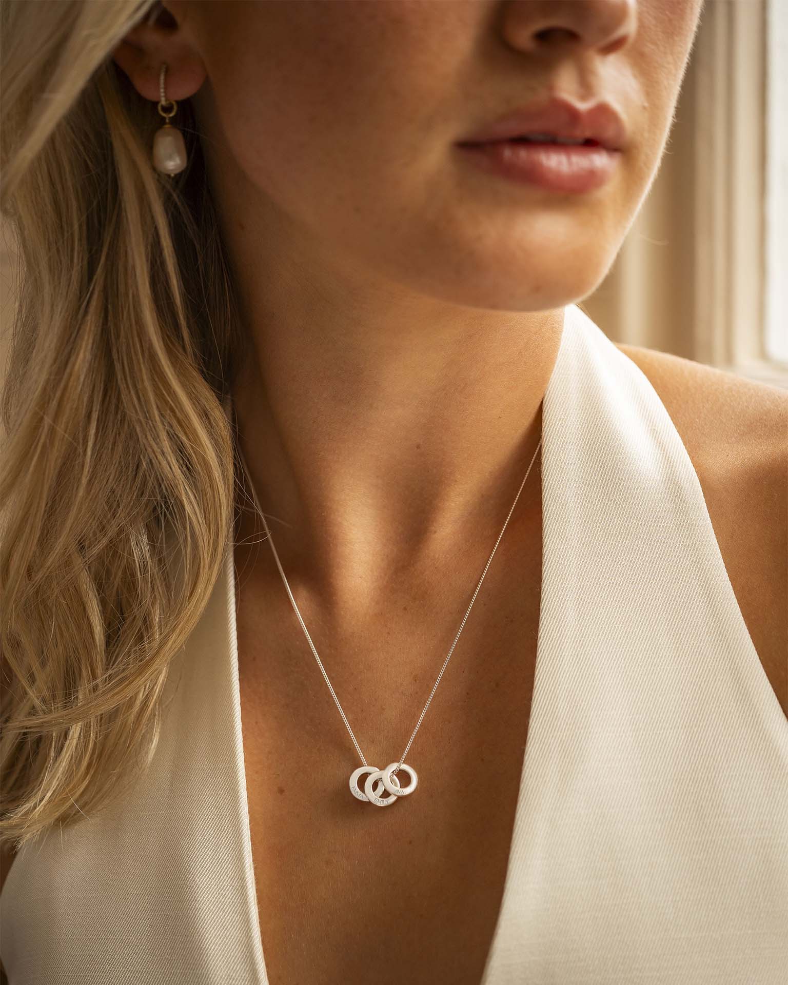 Close-up of a woman wearing a silver necklace with interlocking rings, with a neutral background.