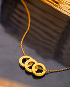 Gold necklace with three interlocking rings engraved with names on a dark surface.