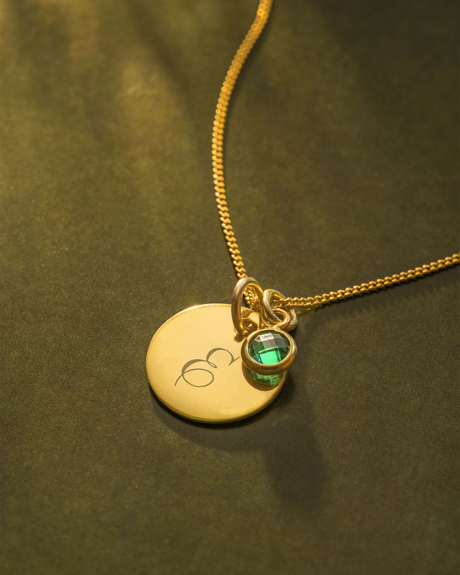 Gold necklace with a round pendant and green gemstone on a green background