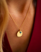 Gold necklace with a pendant featuring a blue gemstone on a person wearing a red garment. | Christmas