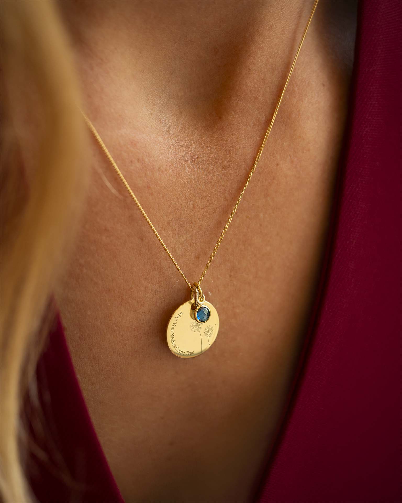 Gold necklace with a pendant featuring a blue gemstone on a person wearing a red garment. | Christmas