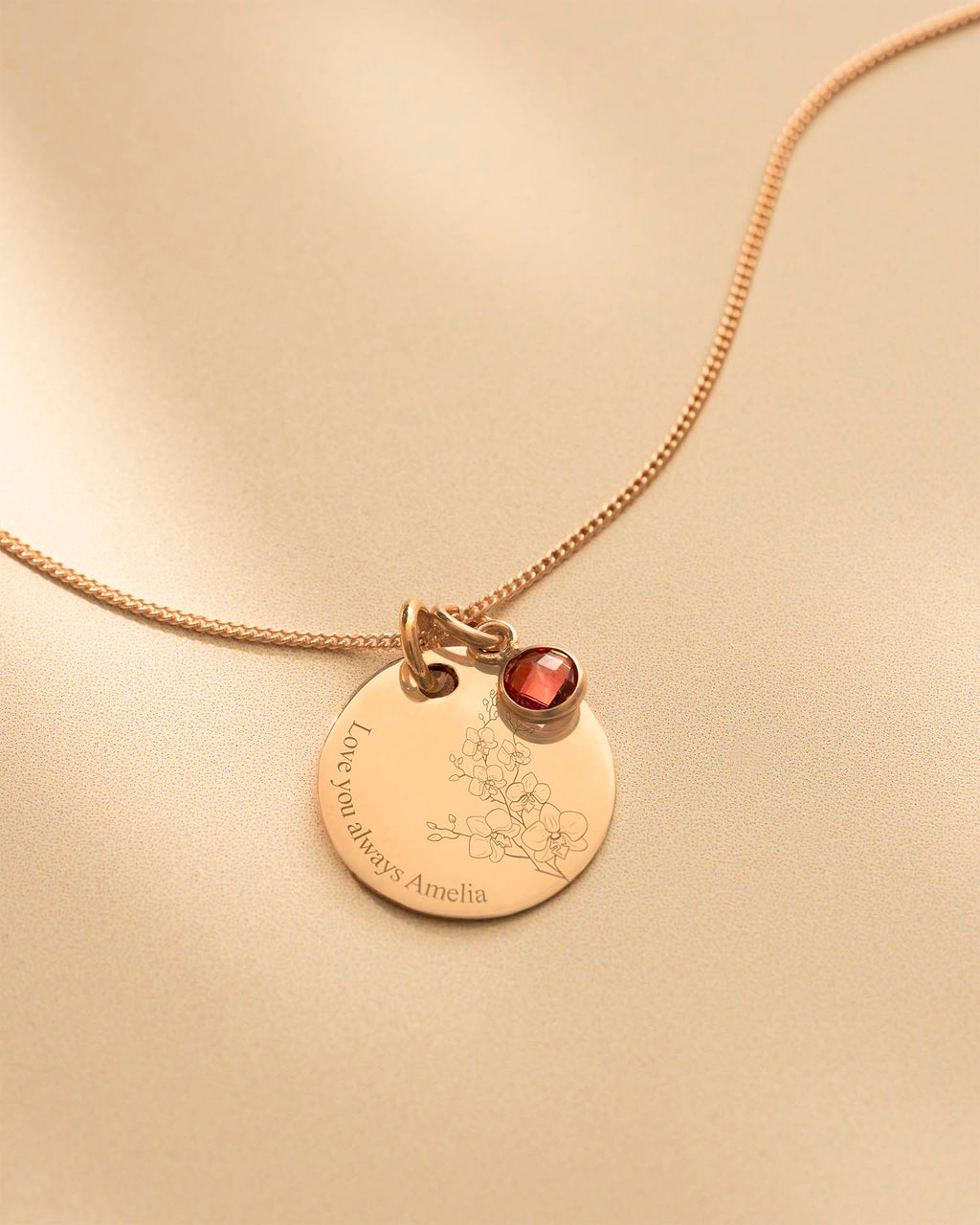 Gold necklace with a round pendant and red gemstone on a beige background