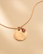 Gold necklace with a round pendant and red gemstone on a beige background