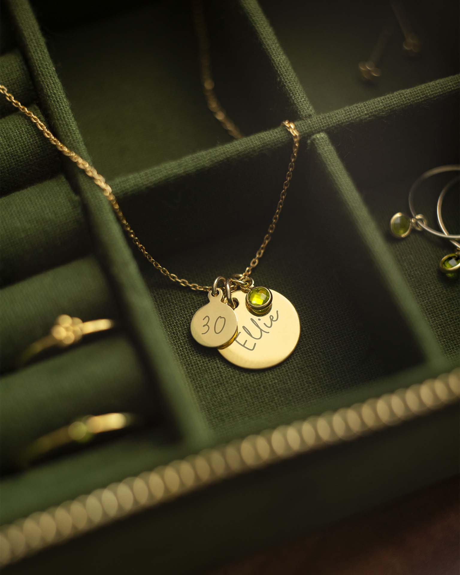 Gold necklace with round pendants and a green gemstone on a green jewelry box.