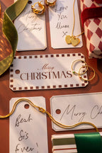 Gold earrings on Christmas-themed gift tags with decorative ribbons.