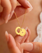Gold necklace with two interlocking rings held by a hand against a blurred background