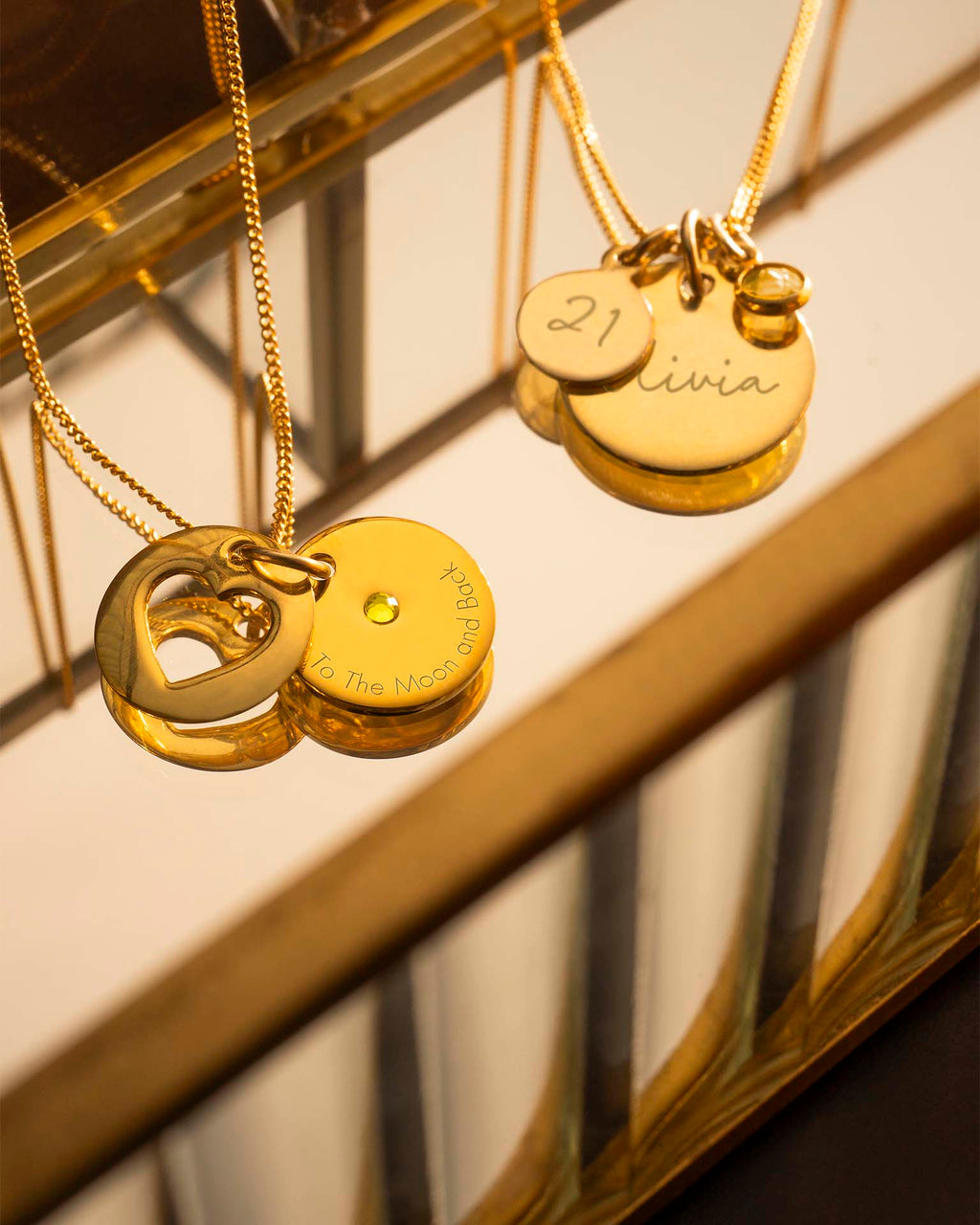 Gold necklaces with engraved pendants on a reflective surface
