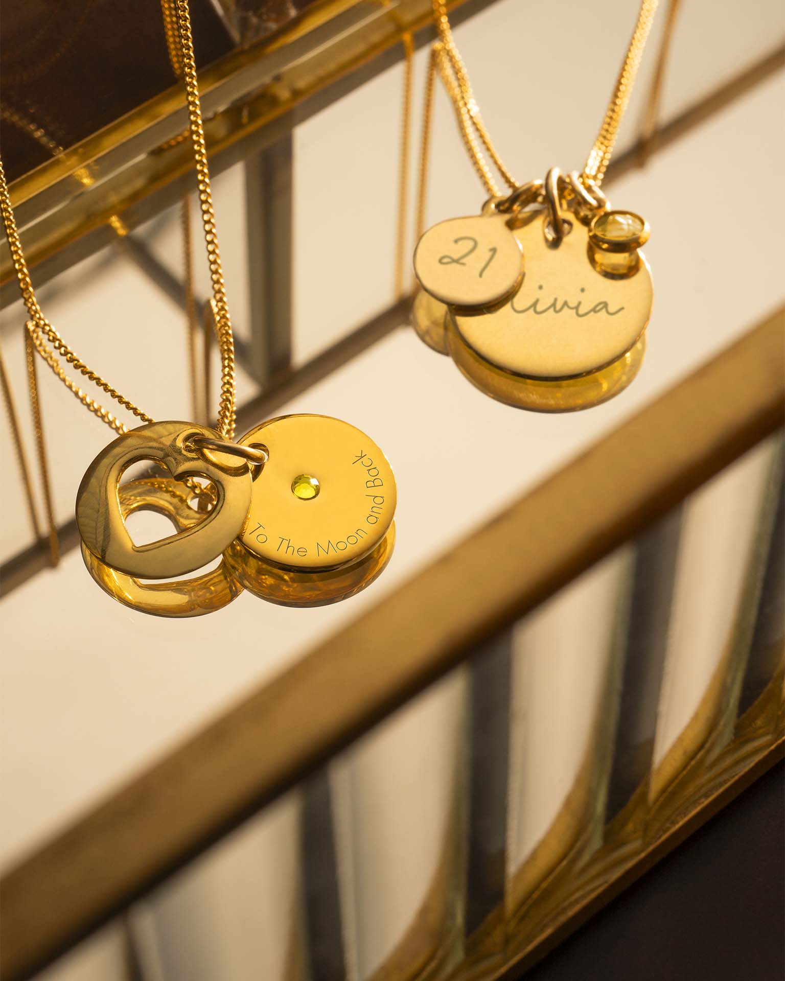 Gold necklaces with engraved pendants on a reflective surface