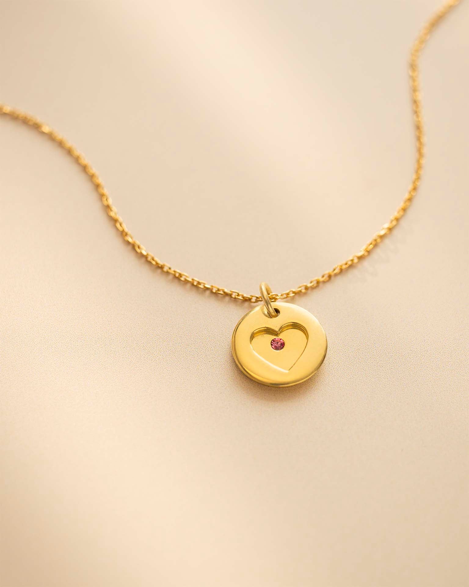 Gold necklace with a heart-shaped pendant on a beige background