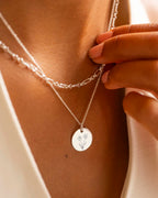 Silver necklace with a floral pendant being adjusted on a person's neck.