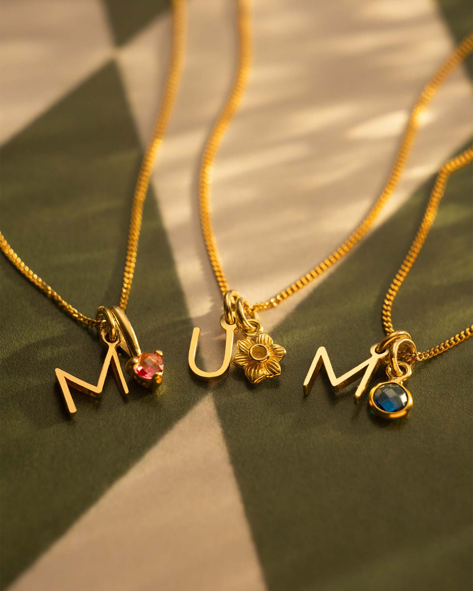 Three gold necklaces with charms on a textured surface