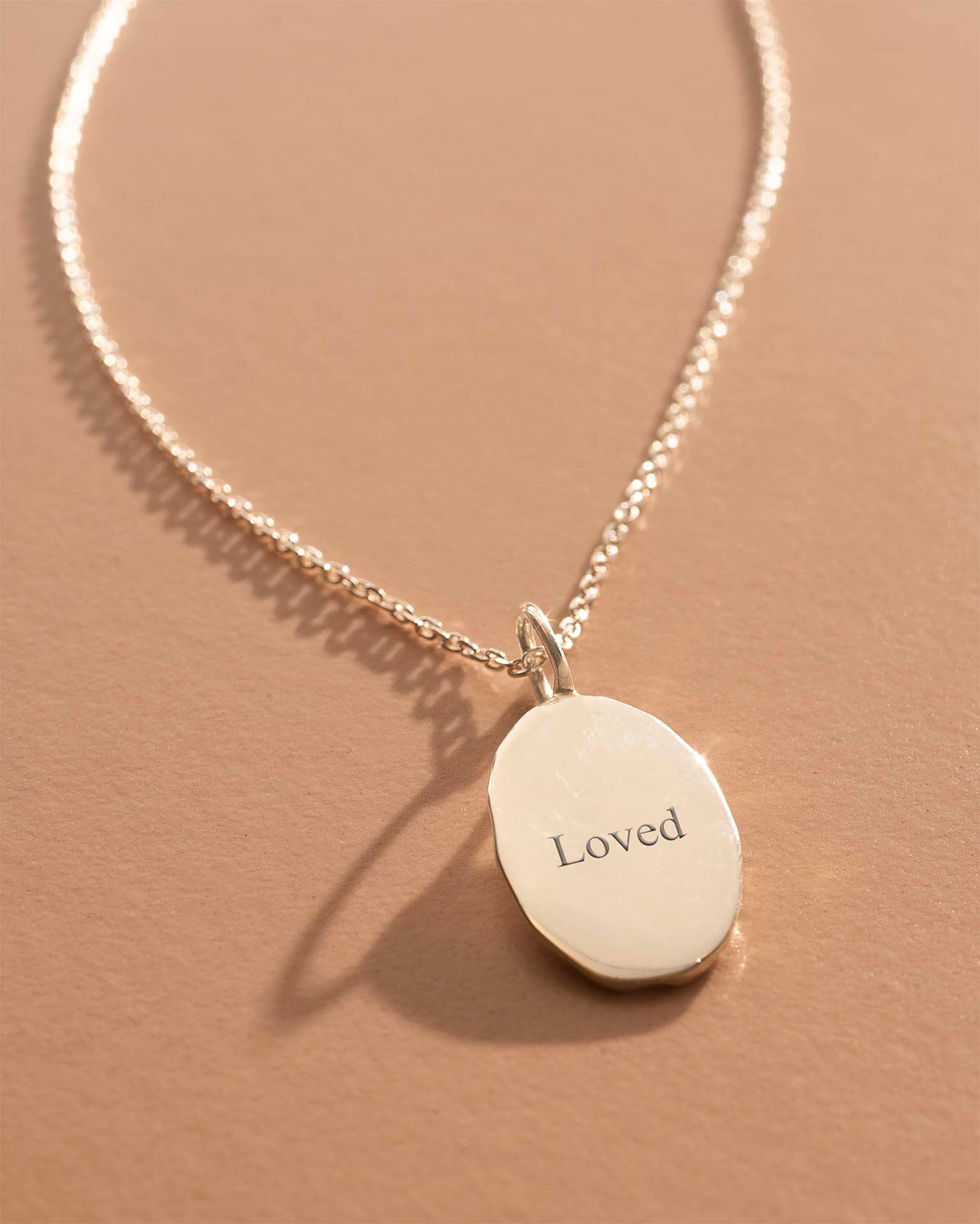 Necklace with a pendant engraved with 'Loved' on a beige background