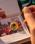Gold necklace held above a box with a picture of some children behind. | Christmas