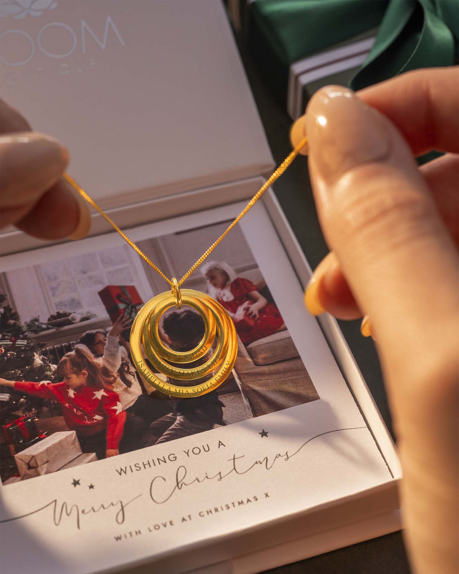 Gold necklace held above a box with a picture of some children behind. | Christmas