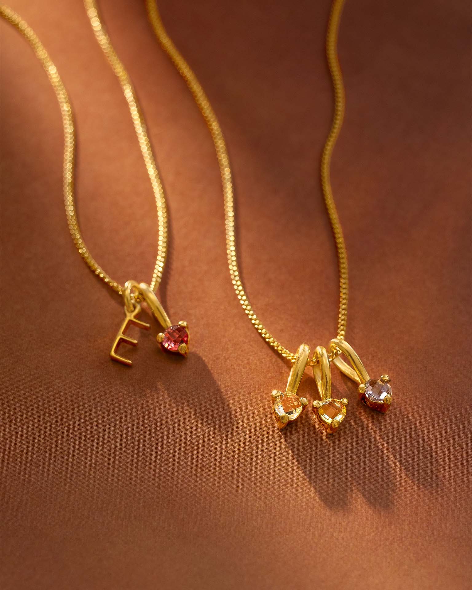Two gold necklaces with small pendants on a brown background