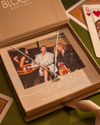 Necklace with a pendant displayed in a box with a photo of three people, on a green surface with playing cards.