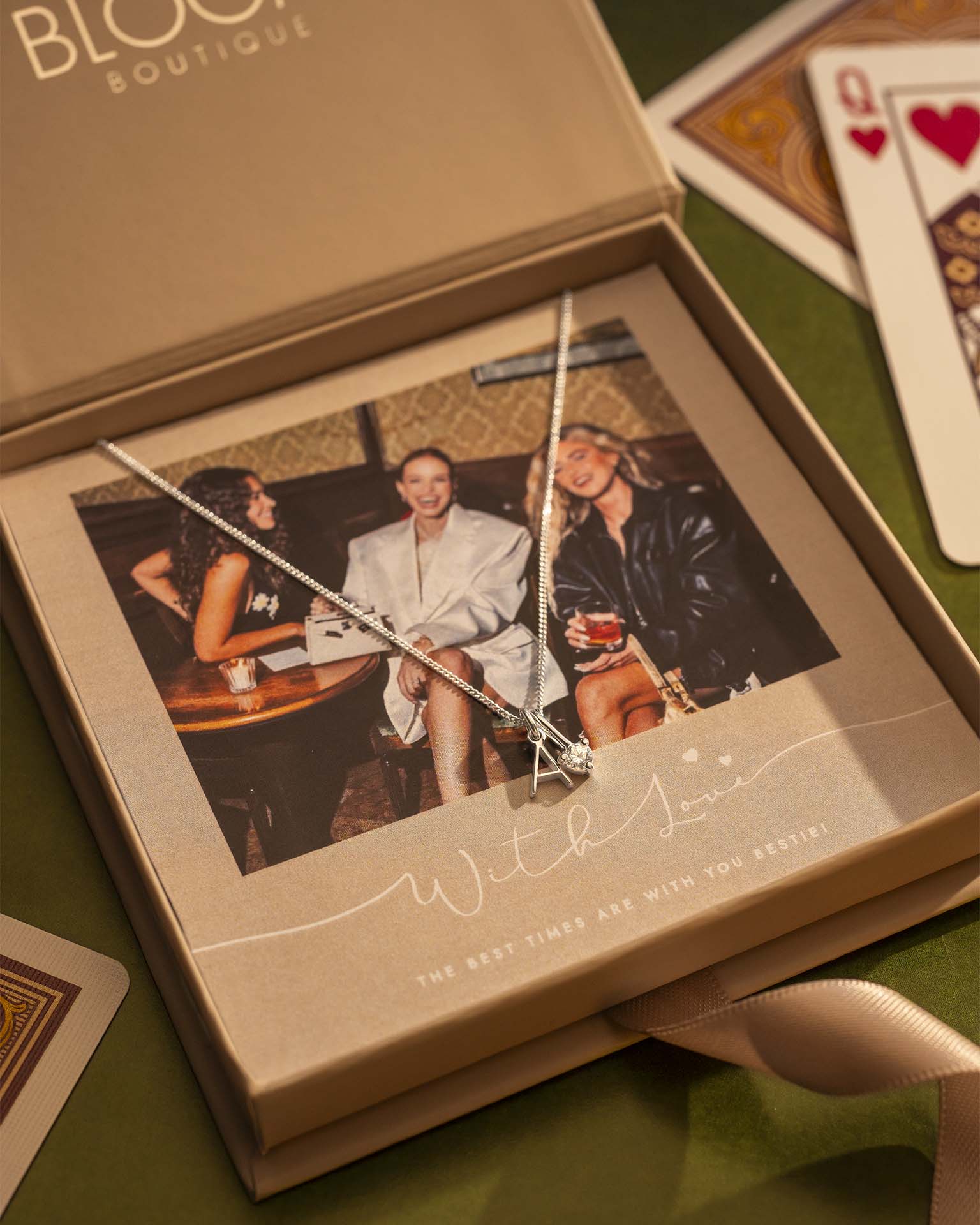 Necklace with a pendant displayed in a box with a photo of three people, on a green surface with playing cards.