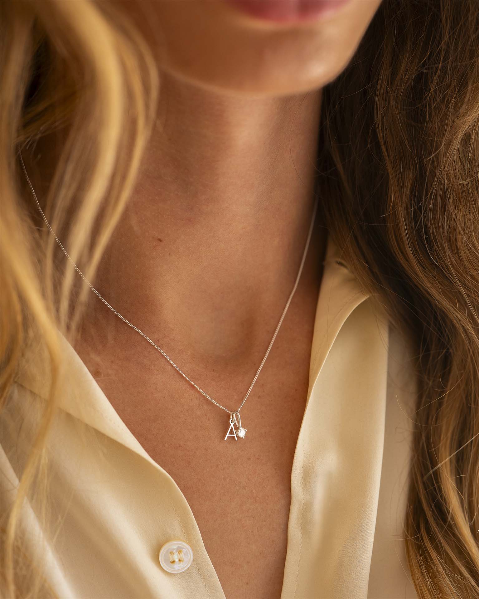 Necklace with a small pendant worn by a person in a beige shirt.