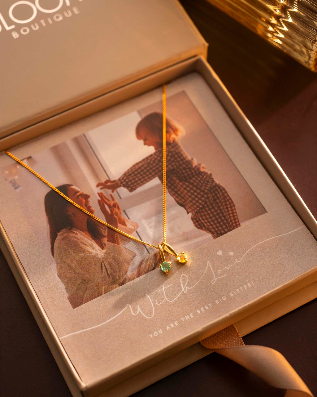 Gold necklace with a heart pendant on a photo of a couple in a box labeled 'BLOOM BOUTIQUE'.