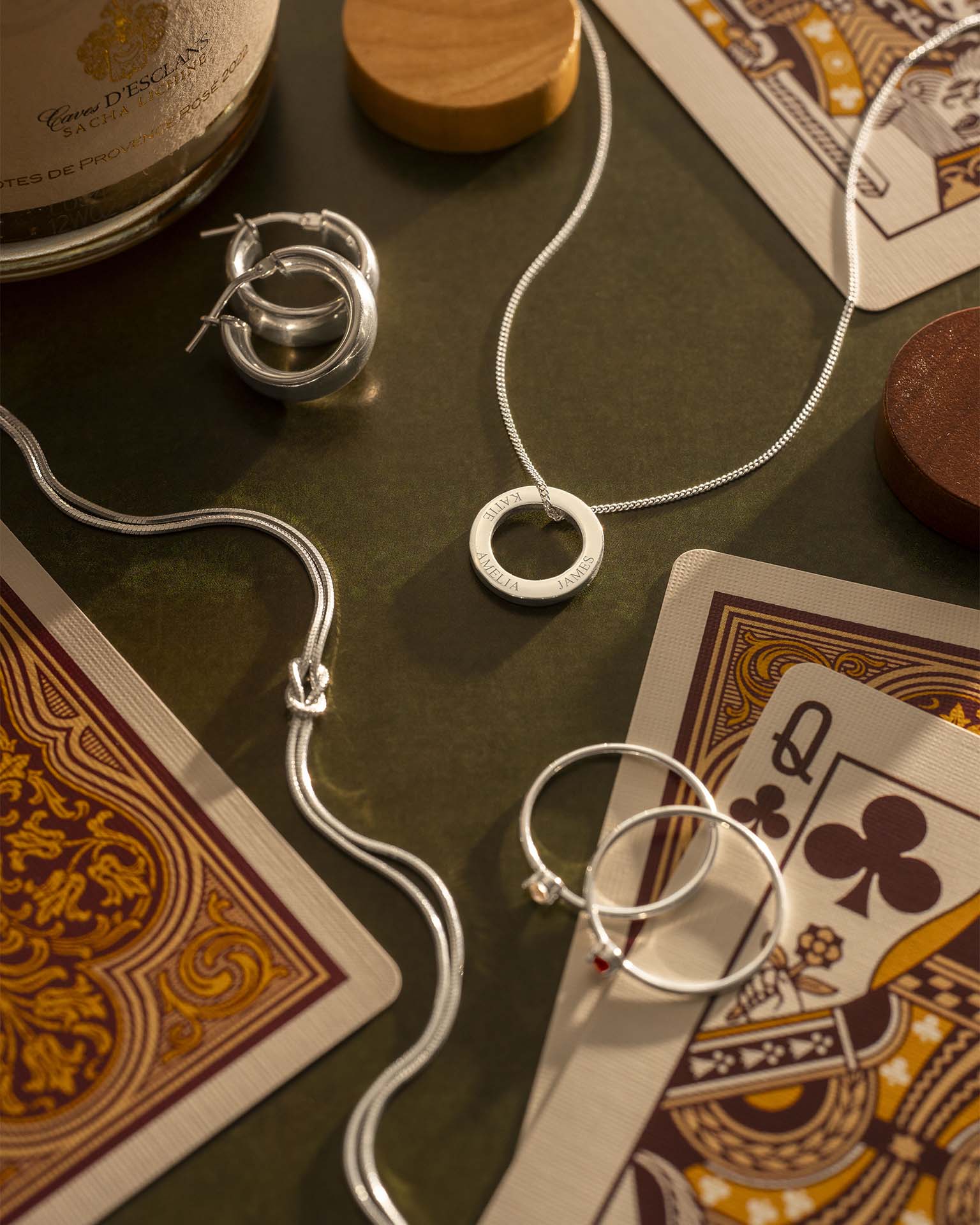 Silver jewelry on playing cards with a bottle of Cognac in the background