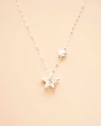 Silver star-shaped necklace with a 'S' pendant on a beige background 