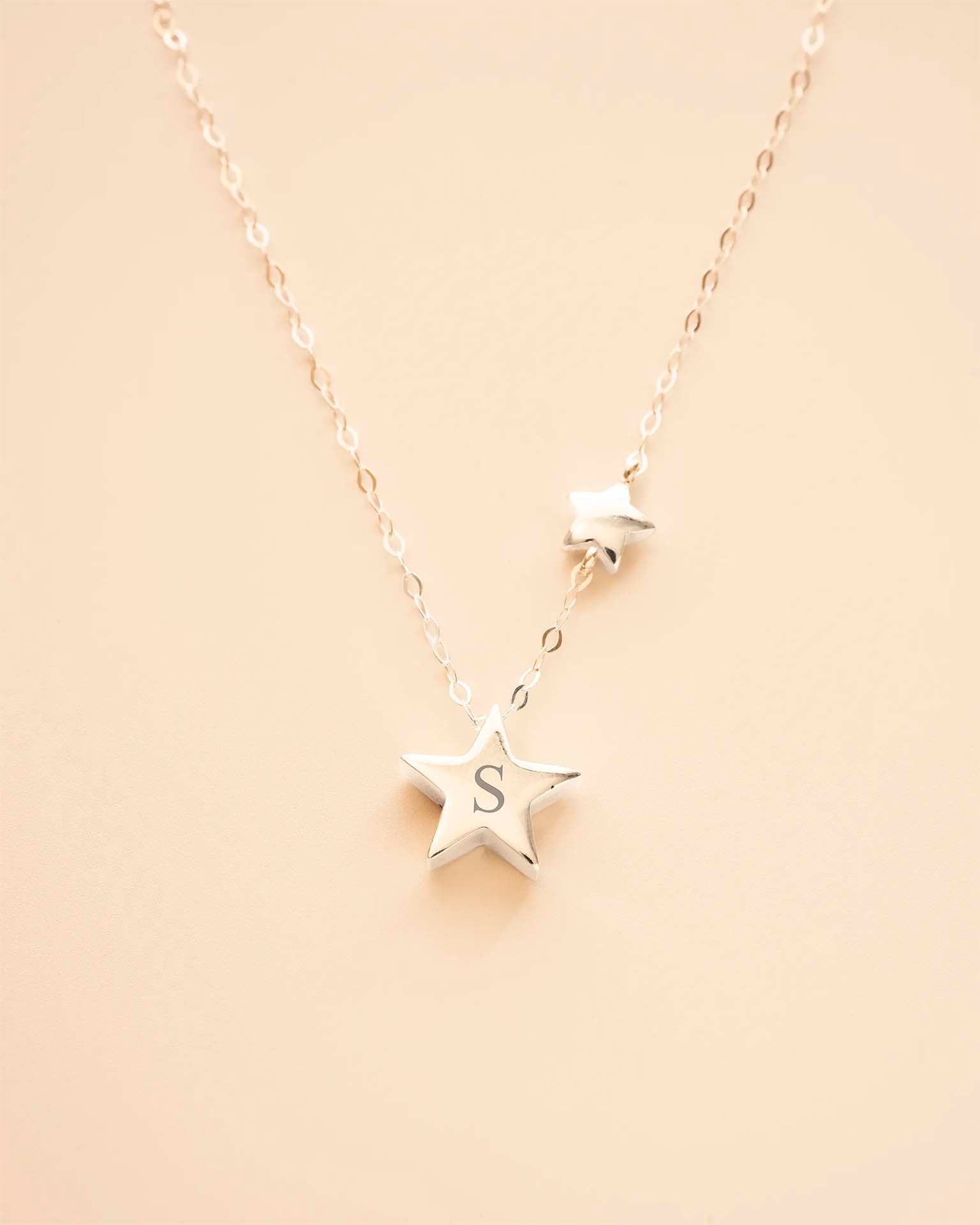 Silver star-shaped necklace with a 'S' pendant on a beige background 