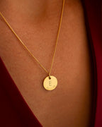 Gold necklace with a round pendant featuring the letter 'E' on a person's neck. | Christmas