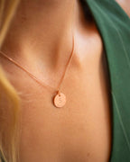 Rose gold necklace with a round pendant on a person wearing a green top.