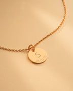 Gold necklace with a round pendant engraved with 'S' and numbers on a beige background
