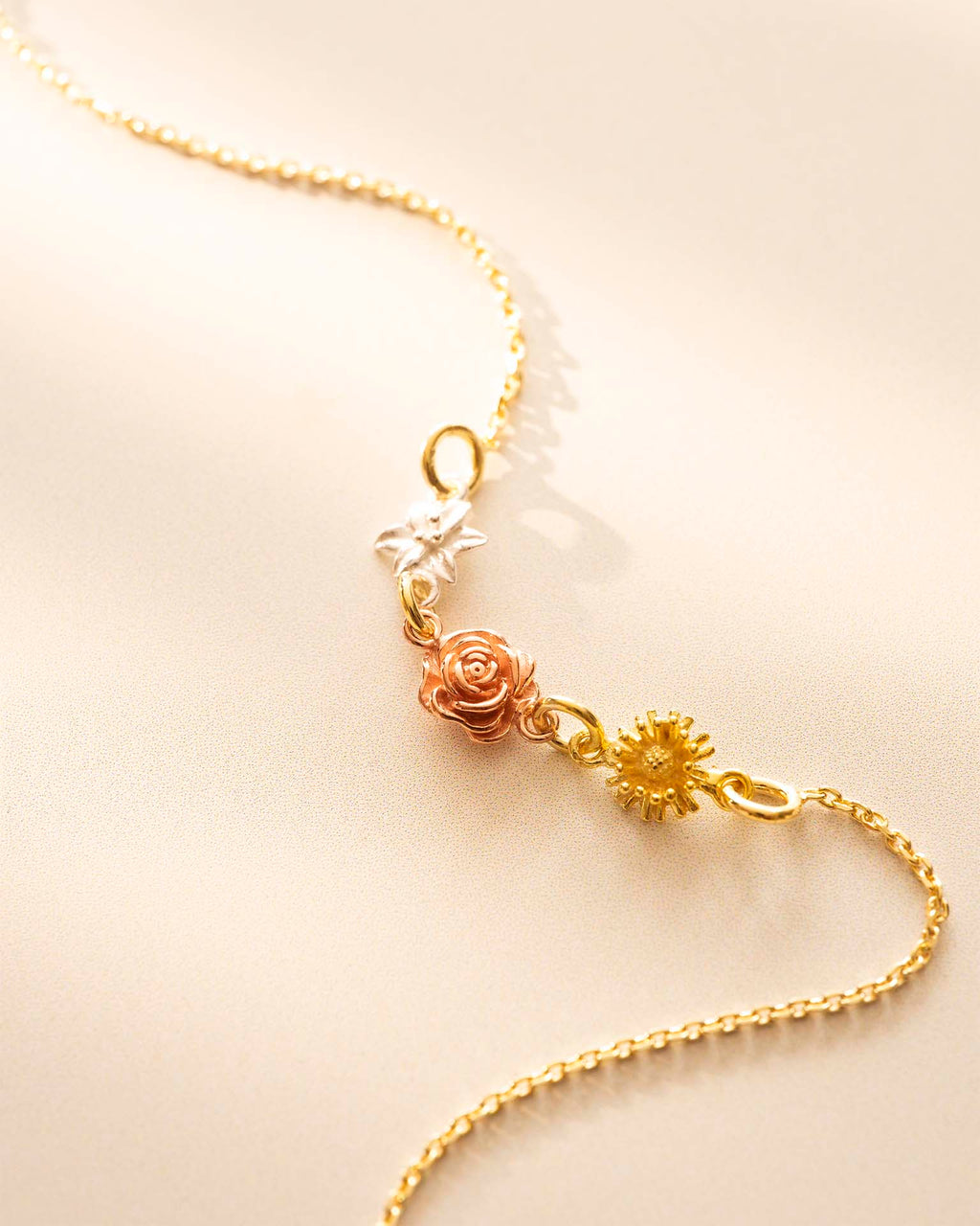 Gold bracelet with floral and star-shaped charms on a beige background